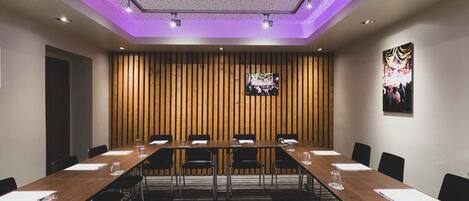 Un salón de conferencias con una larga mesa, sillas, una pantalla de televisión y un papel tapiz decorativo.