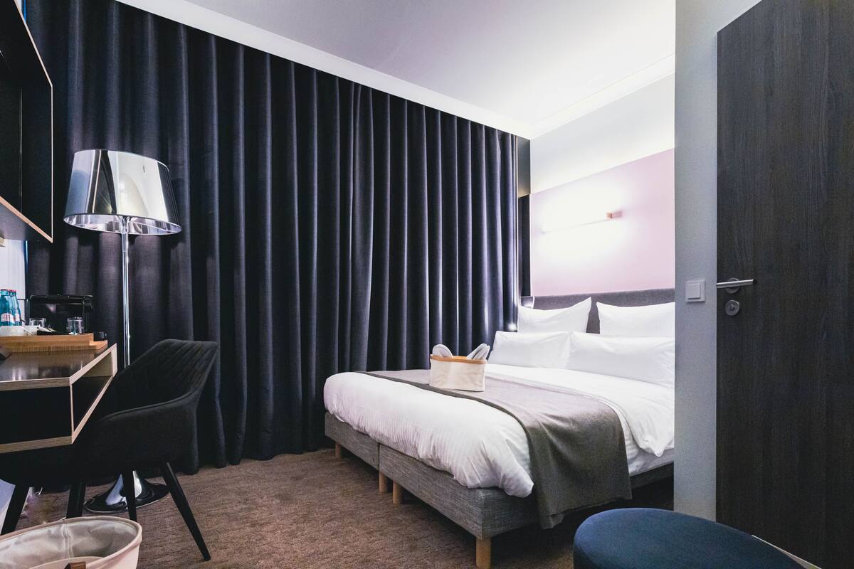 A hotel room with a bed, a desk with a lamp, a chair, and a small table with a coffee machine.