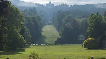 Ein Park mit gepflegten Rasenflächen, einer Statue und einem Gebäude in der Ferne.