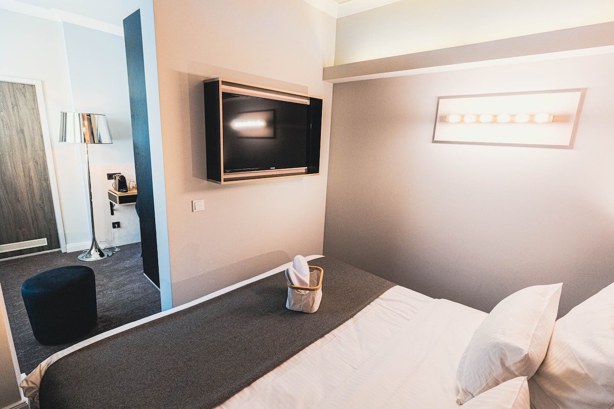 A hotel room with a bed, a TV mounted on the wall, a bedside table, and a lamp.