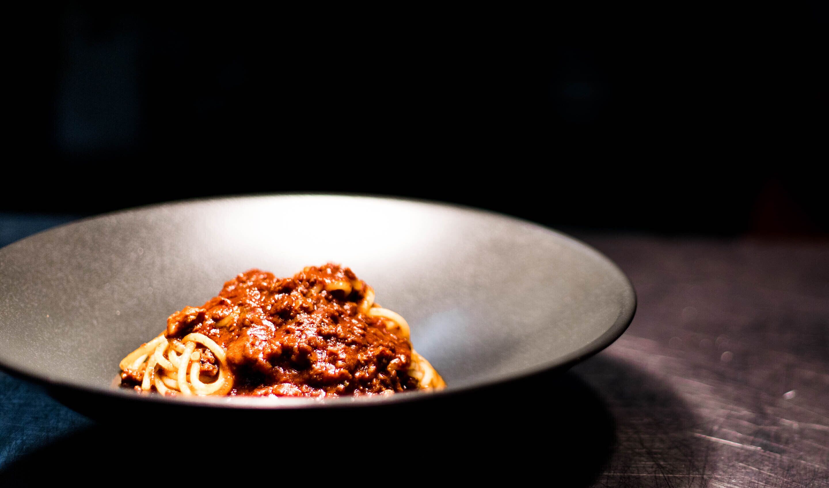 A plate of spaghetti with a rich red sauce, served on a dark plate.