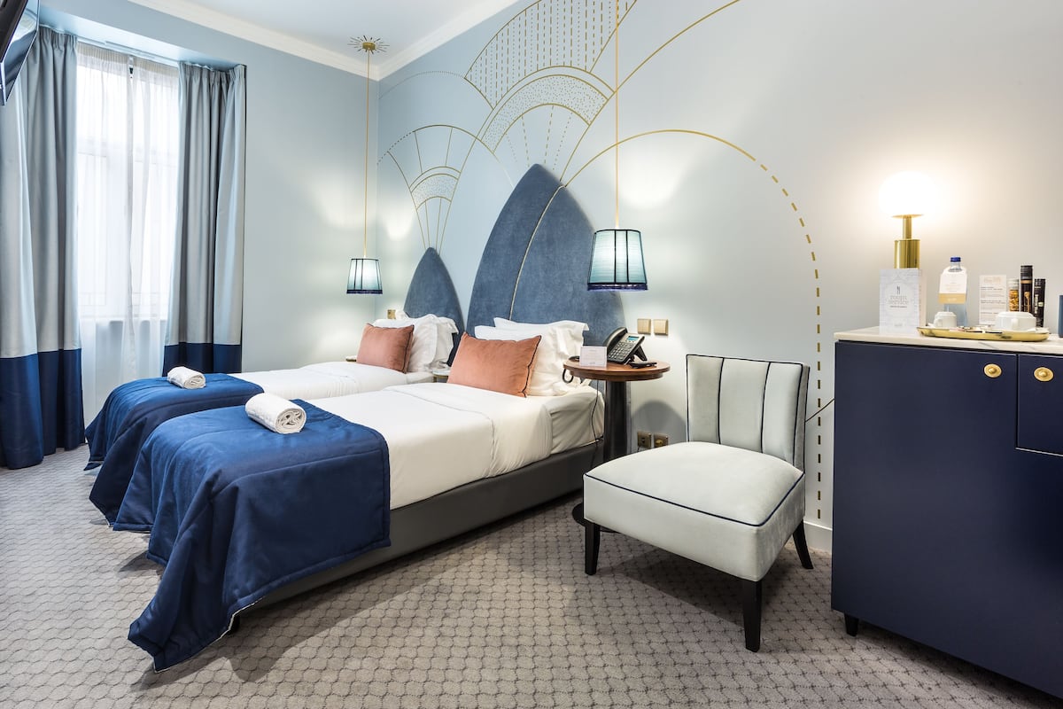 Habitación de hotel con dos camas, una mesita con un teléfono, un armario y una pared con iluminación decorativa.
