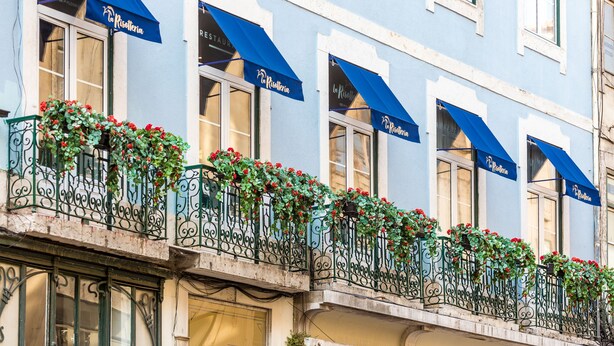 Un edificio con diversi balconi decorati con fiori rossi e tende parasole blu.