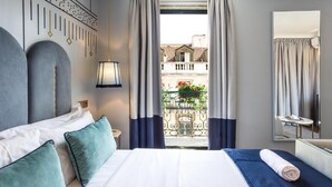 Camera d'albergo con un letto grande, un tavolino, uno specchio e un balcone con ringhiera e qualche pianta.