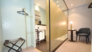 Un bagno moderno con divisorio in vetro, portasci asciugamani, una sedia e un piccolo tavolo con lampada.