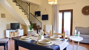 A dining area with a table set for four, a staircase, a television, and a sofa. - Elianthos Villa (Apokoronas)