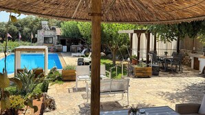 A poolside area with a thatched umbrella, outdoor furniture, and a stone pathway. - Elianthos Villa (Apokoronas)