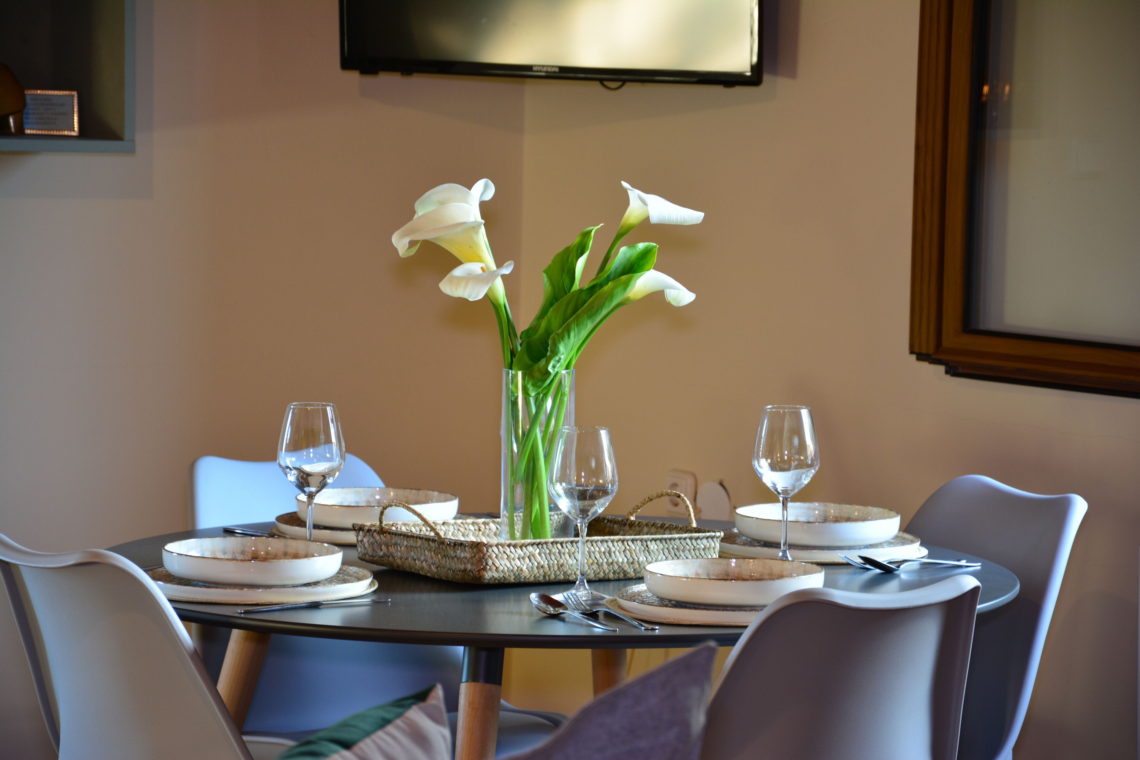 Una mesa de comedor dispuesta con platos, cubiertos y un florero con flores.
