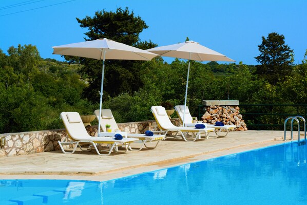 Una piscina al aire libre, sombrillas, sillones reclinables de piscina