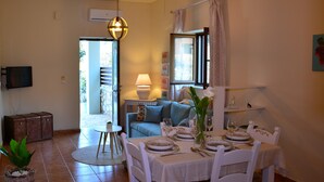 A dining area with a table set for four, a sofa, a lamp, and a television mounted on the wall. - Elianthos Villa (Apokoronas)