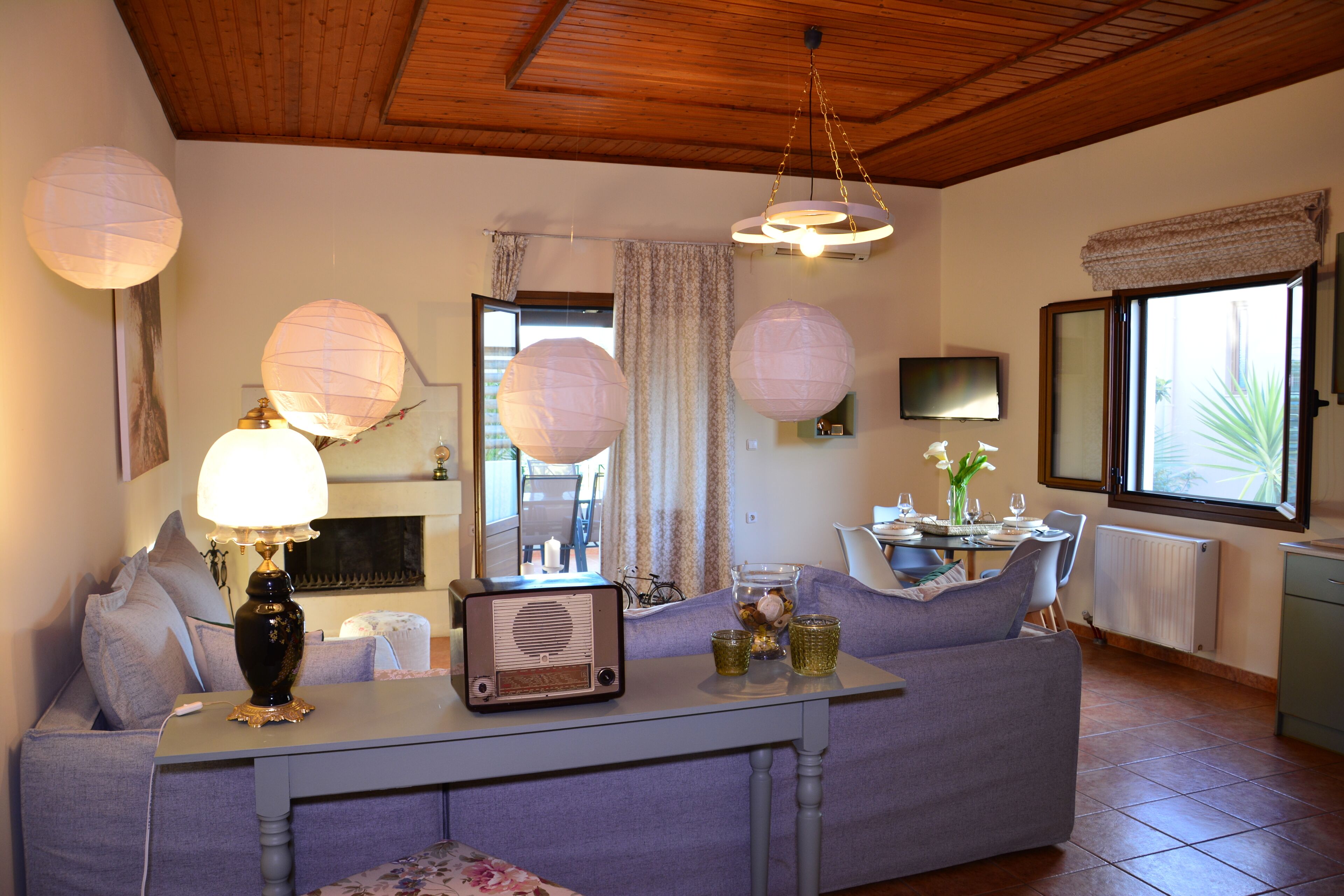 Un salon comprenant un canapé, une table avec une radio, des lanternes décoratives en papier, un téléviseur et une fenêtre avec des rideaux.