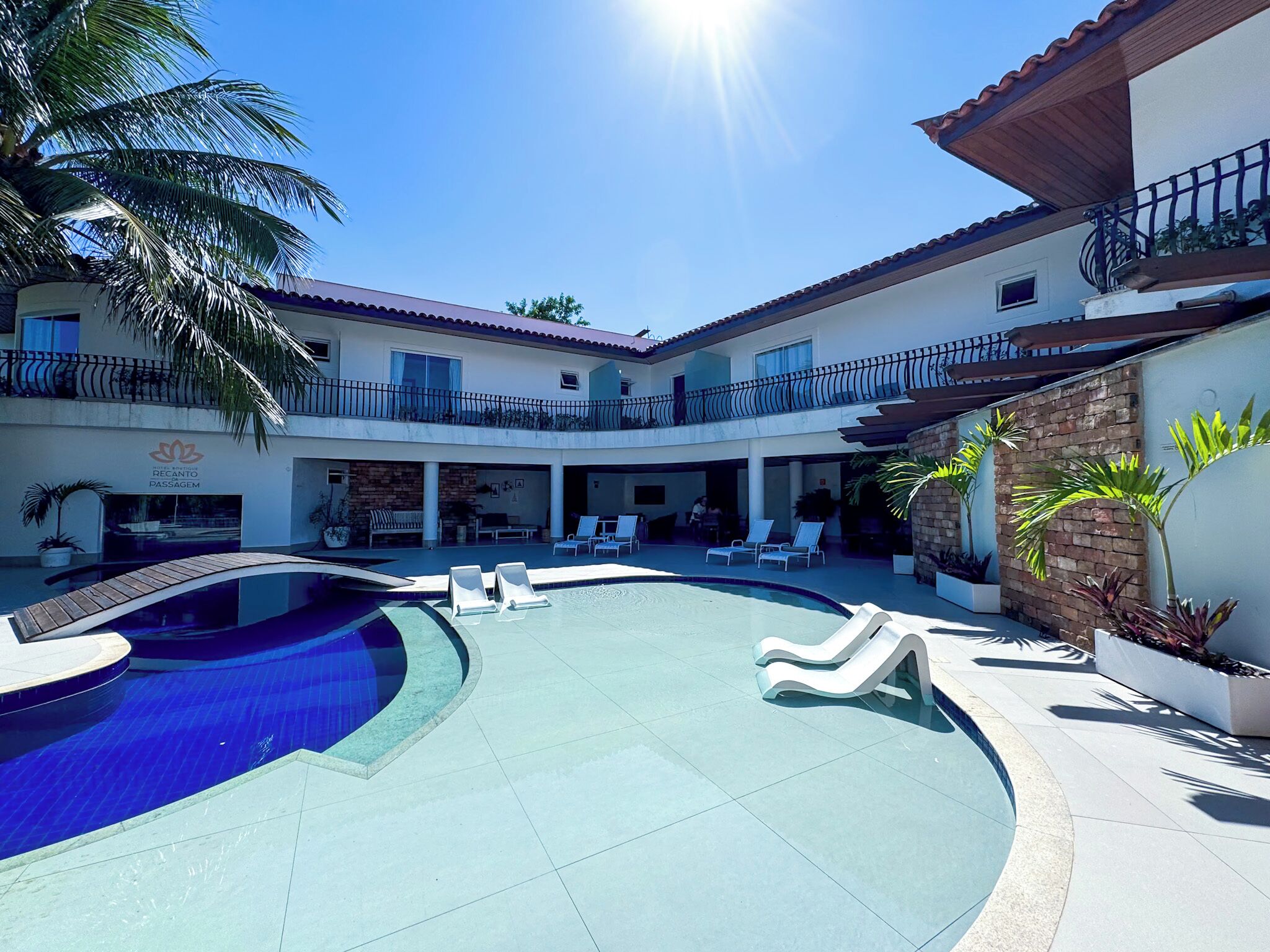 Un área de piscina con sillones de descanso, una palmera y un edificio con un cartel que dice 'Recanto Passage'.