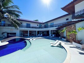 Un área de piscina con sillones de descanso, una palmera y un edificio con un cartel que dice 'Recanto Passage'.