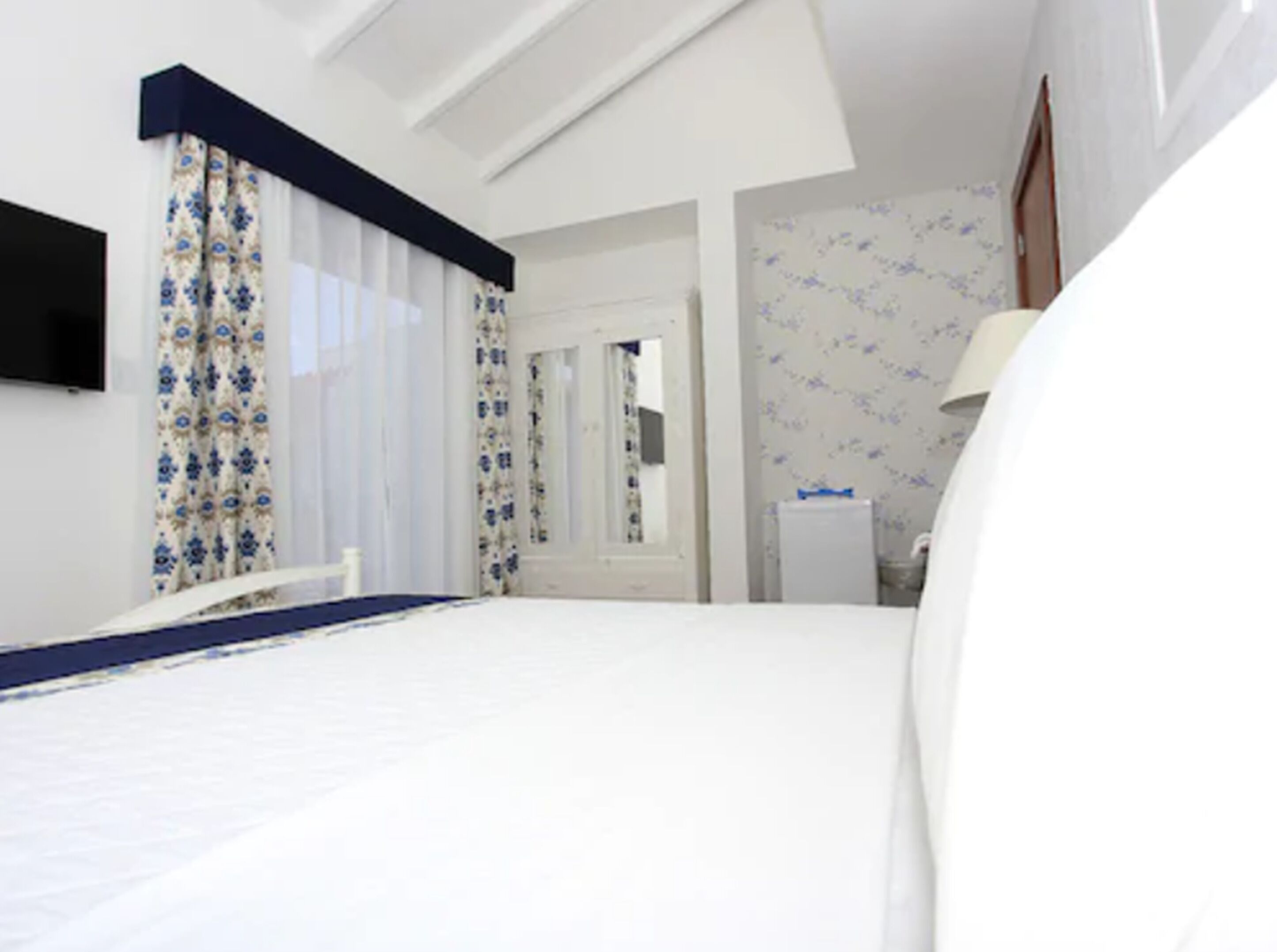 Quarto de hotel com uma cama grande, mesa de cabeceira, espelho e guarda-roupa.