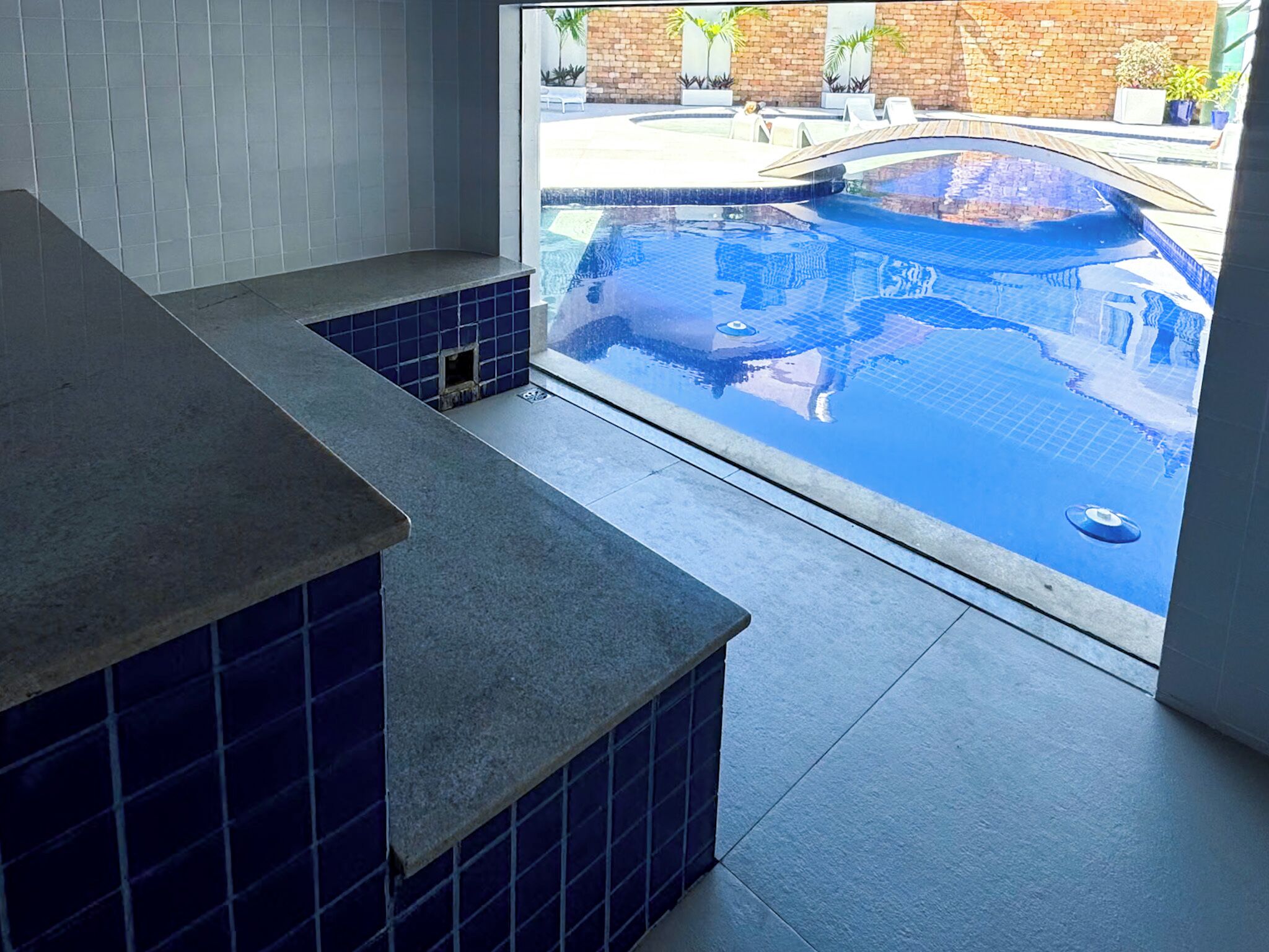 A modern bathroom with a large bathtub, a shower area, and a view of an outdoor swimming pool.