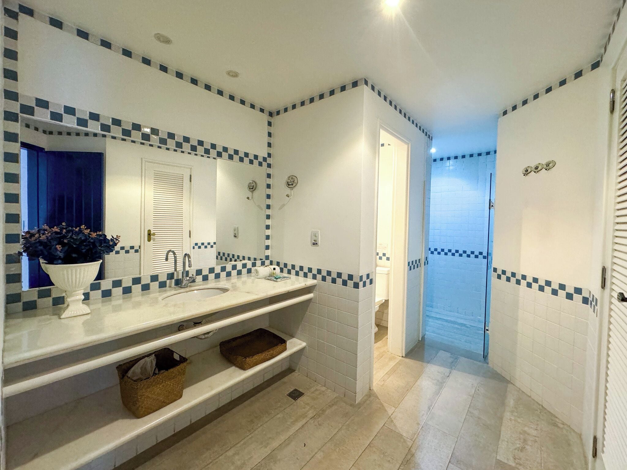 A bathroom with a white sink, a mirror, and a blue checkered tile border. There is a plant on the counter and a towel hanging on the wall.