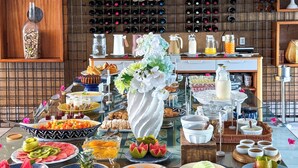 Un bufé con diversos alimentos, una estantería para vinos y un jarrón decorativo con flores.