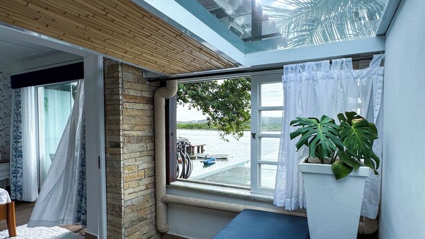 Una habitación acogedora con vistas a un lago, un ventanal con cortinas, techo de madera y una planta en maceta.