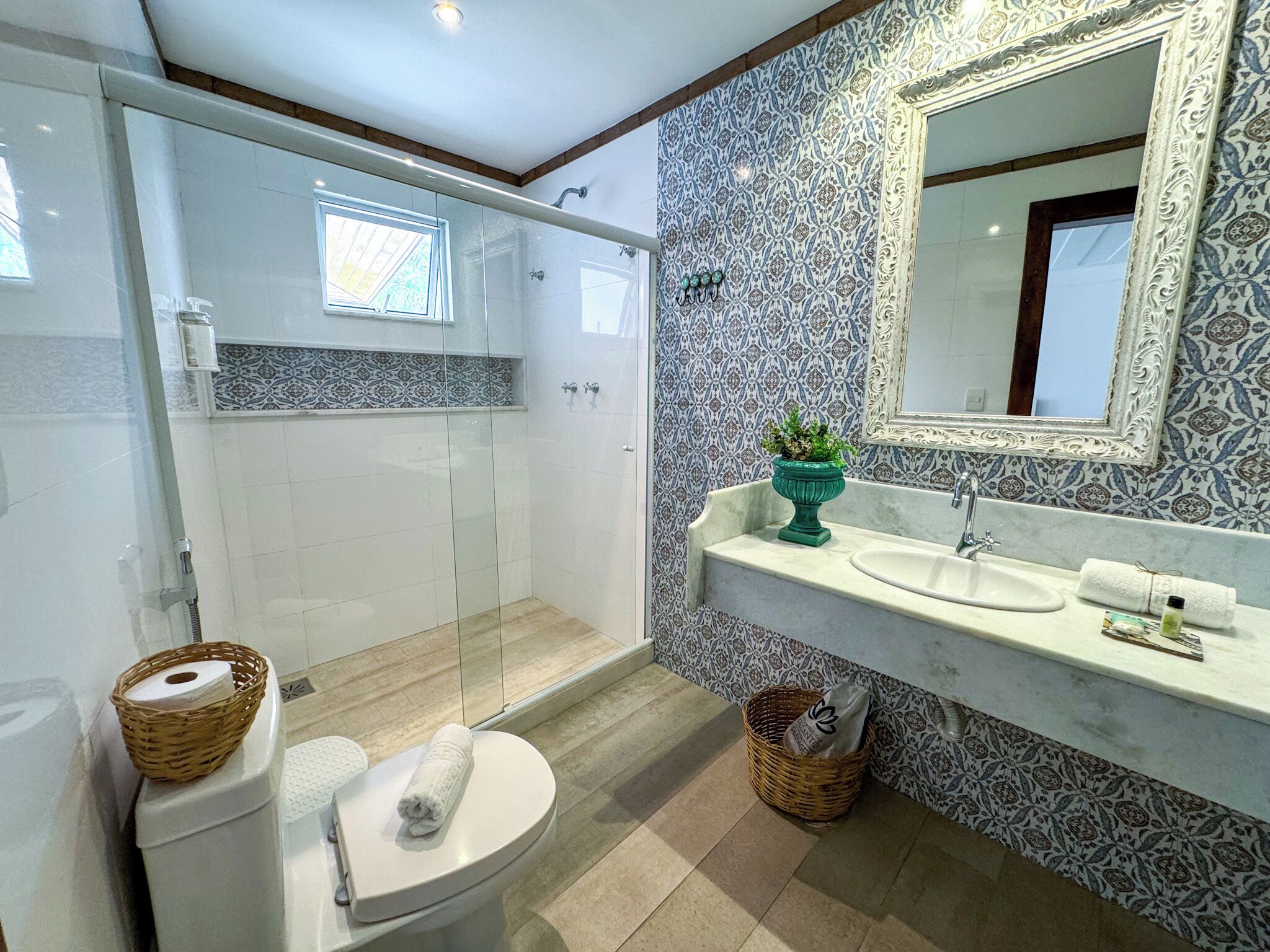 A modern bathroom with a glass-enclosed shower, a toilet, a sink with a mirror, and patterned tiles.