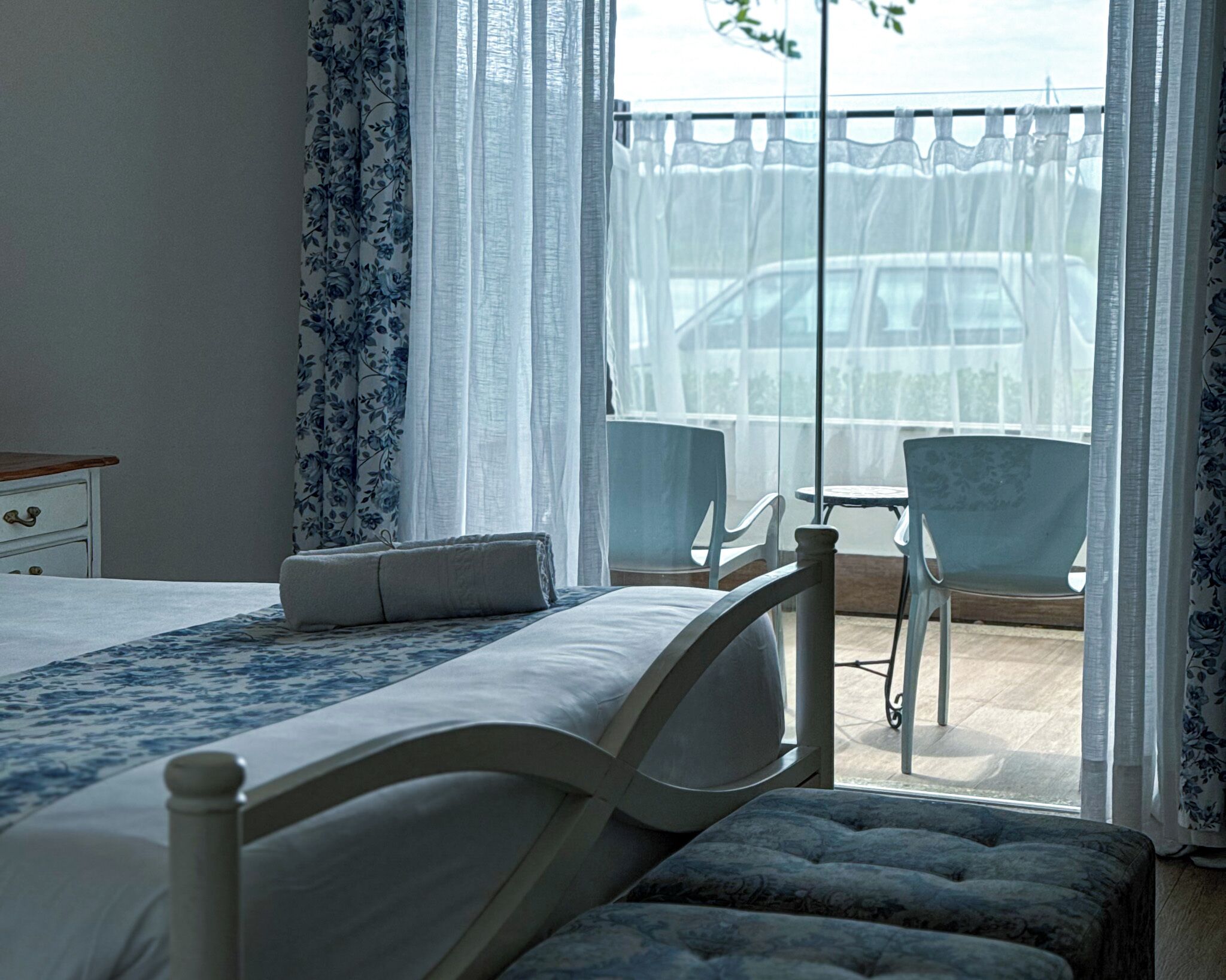 A bedroom with a bed, a bench, and a balcony with chairs and a table.
