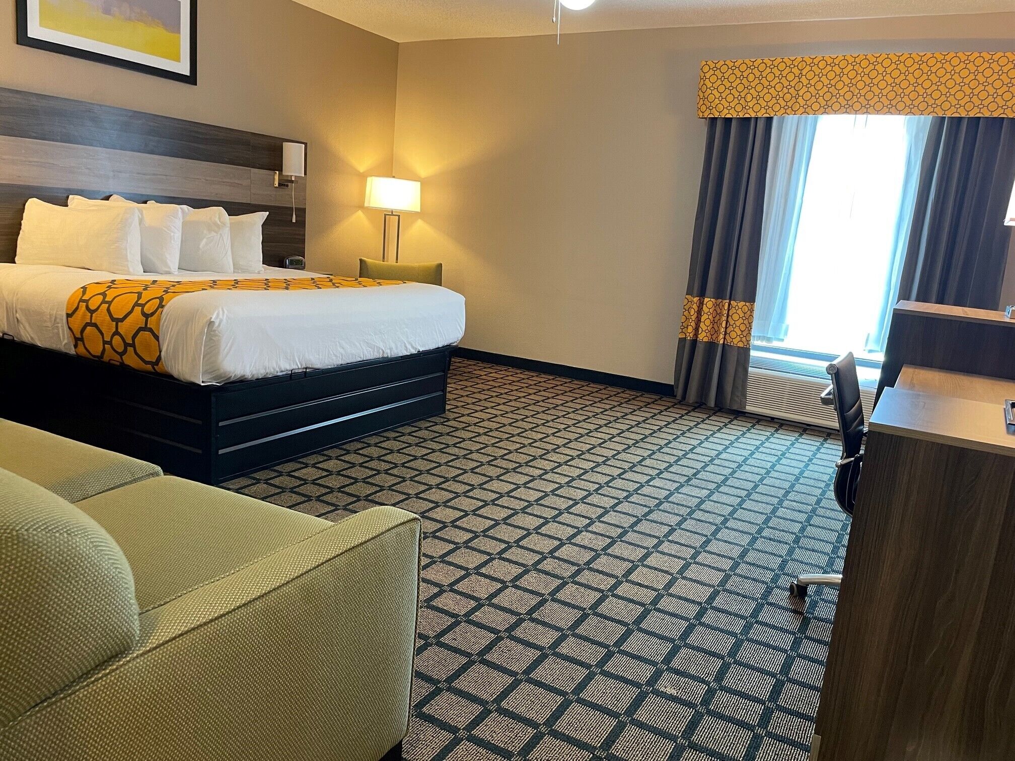 A hotel room with a bed, a desk, a chair, and a patterned carpet.