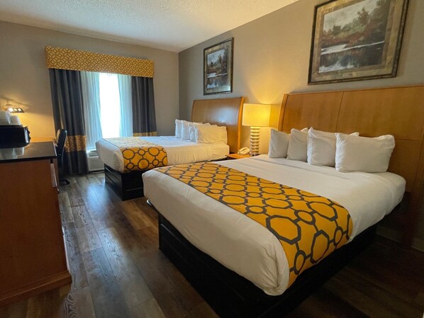A hotel room with two beds, a desk, a lamp, and a painting on the wall.
