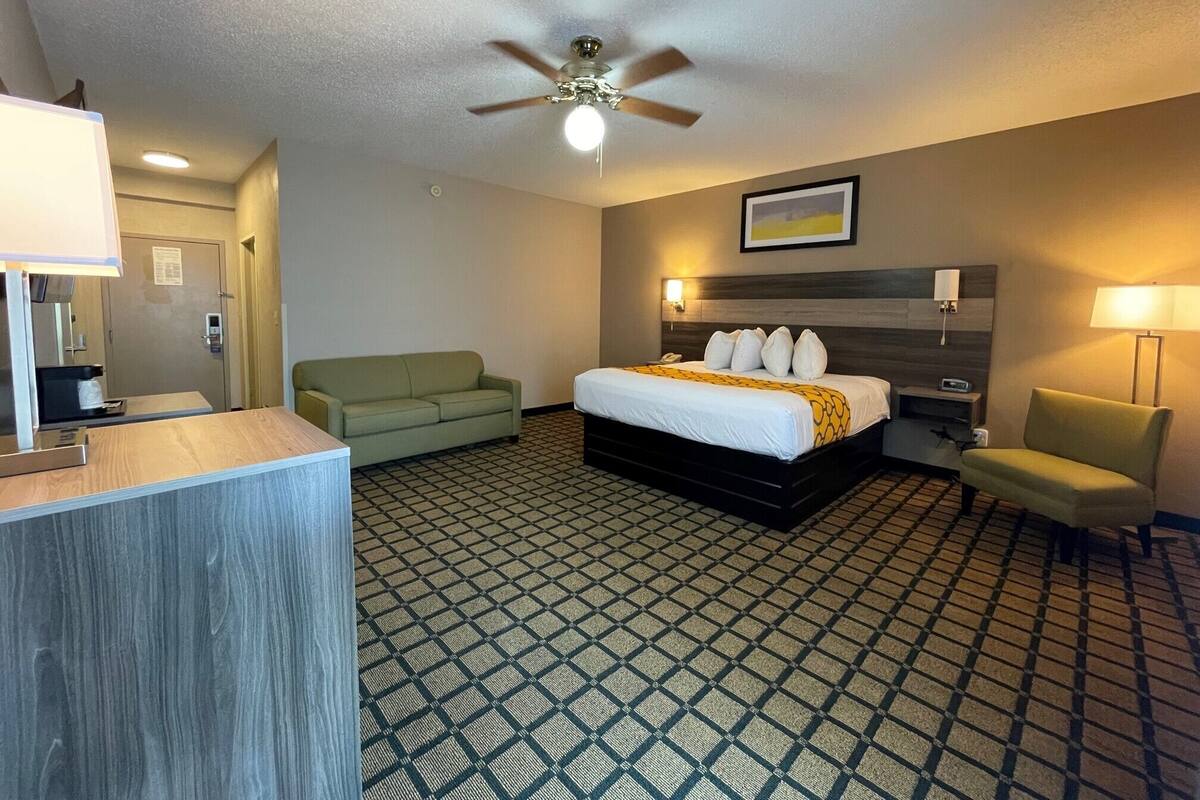 Habitación de hotel con cama, sofá verde, escritorio, ventilador de techo y piso estampado.