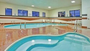 Una amplia piscina interior con varias pistas, suelo de baldosas y ventanas a lo largo de las paredes.