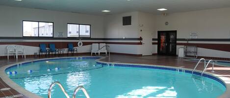 An indoor swimming pool with clear lane markings, a Coca-Cola refrigerator, and a caution sign for slippery floors.