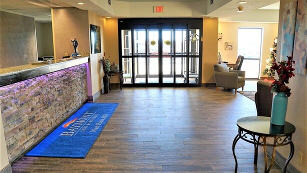 Zona de recepción de hotel con alfombra azul, mostrador de recepción y área de espera con sillas y una mesa.