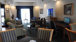 Habitación de hotel con sala de estar, una mesa de comedor, televisor y escritorio con computadora.