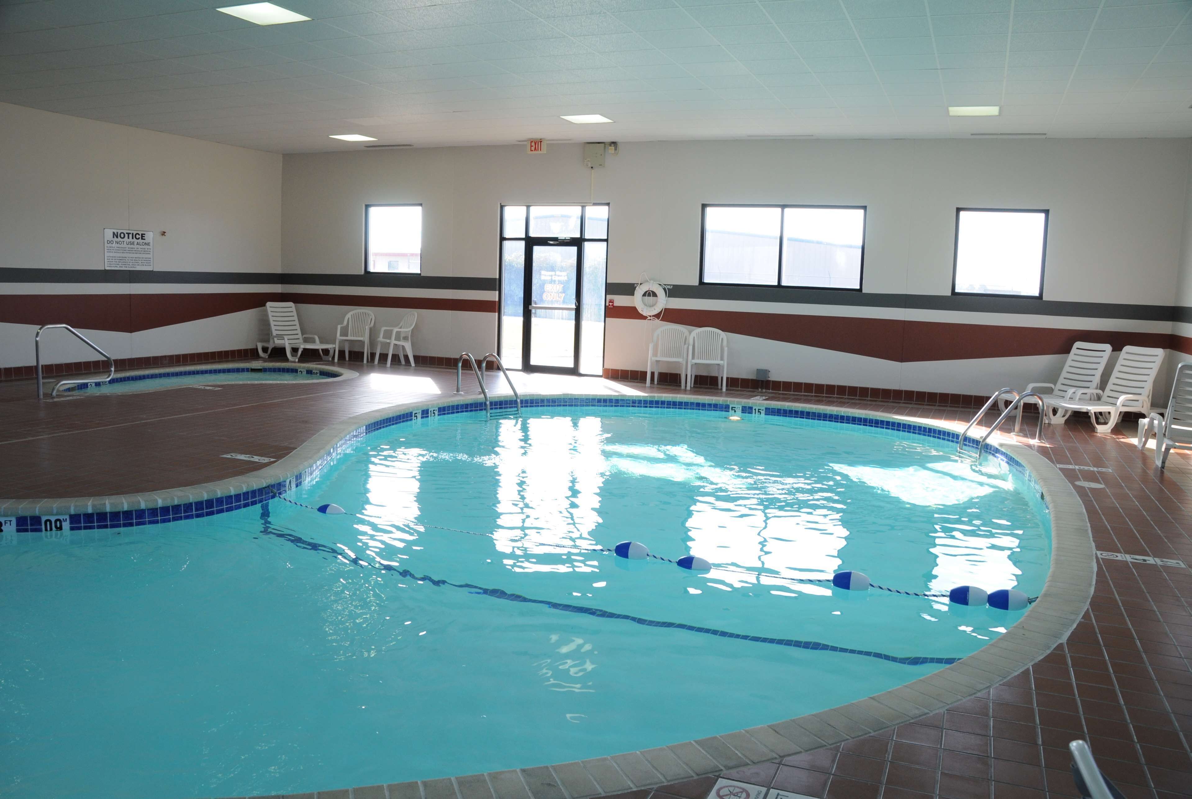 Una piscina cubierta con carriles delimitados, una escalera de piscina y varias sillas de descanso alrededor del borde.