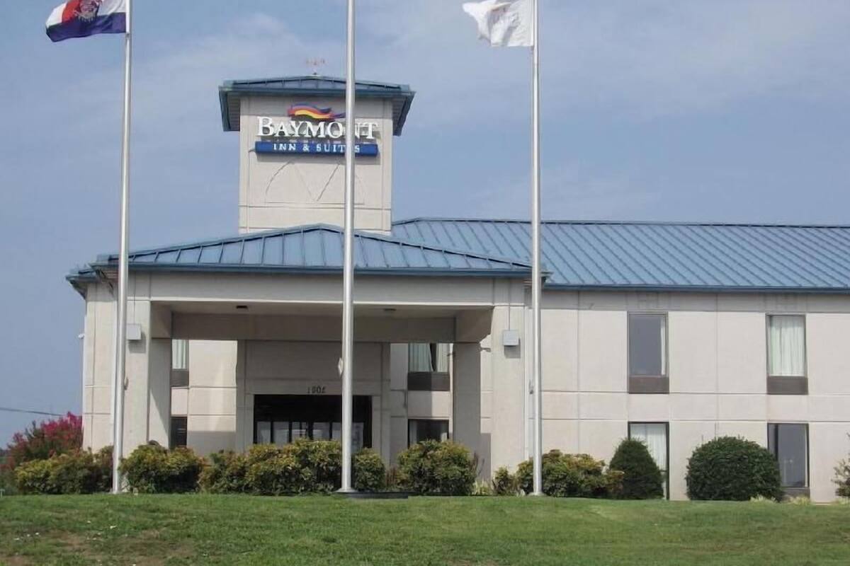 Un hotel llamado 'Baymont Inn & Suites' con un letrero llamativo, techo azul y un asta de bandera con banderas.