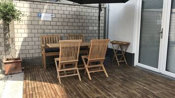 A wooden deck with a table and chairs, a potted plant, and a black umbrella.