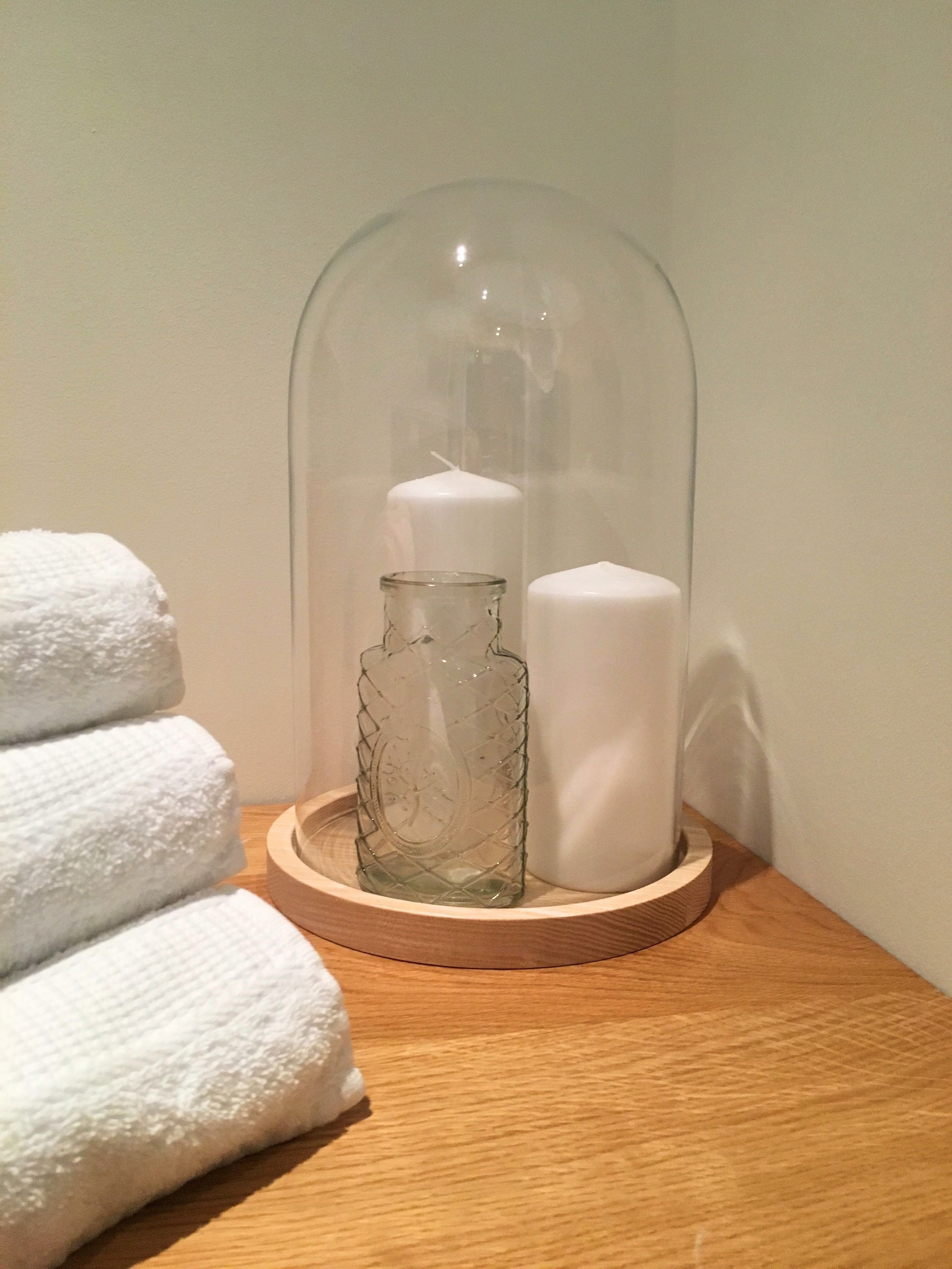 A wooden tray with a glass bottle, a white candle, and folded towels on a wooden surface.