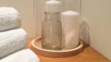 A wooden tray with a glass bottle, a white candle, and folded towels on a wooden surface.