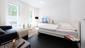 A modern hotel room with a bed, a sofa, a TV, and a lamp. - The Apartment Central (Mainz)