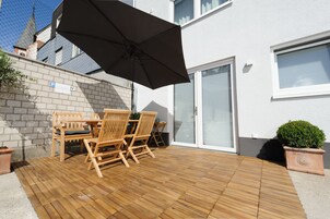 Un patio con mobiliario de madera y un paraguas negro.
