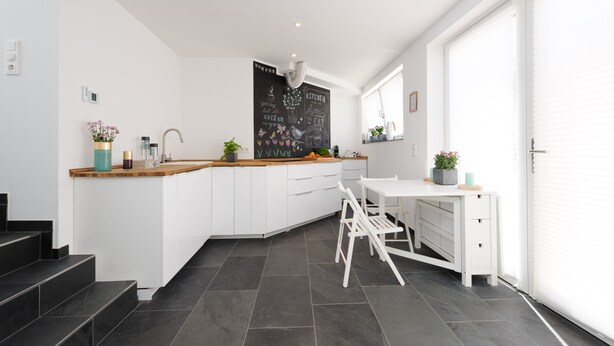 A modern kitchen with a white countertop, wooden cabinets, and a chalkboard wall with kitchen-related phrases. - The Apartment Central (Mainz)