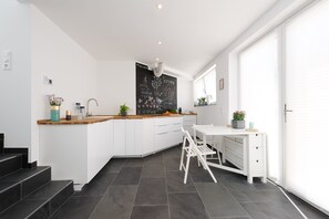 Une cuisine moderne avec un plan de travail blanc, des armoires en bois et un mur noir où sont écrites des expressions liées à la cuisine.