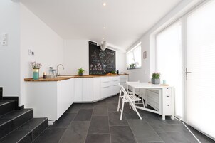 Una cocina moderna con encimera blanca, armarios de madera y una pared de pizarra con frases relacionadas con la cocina.