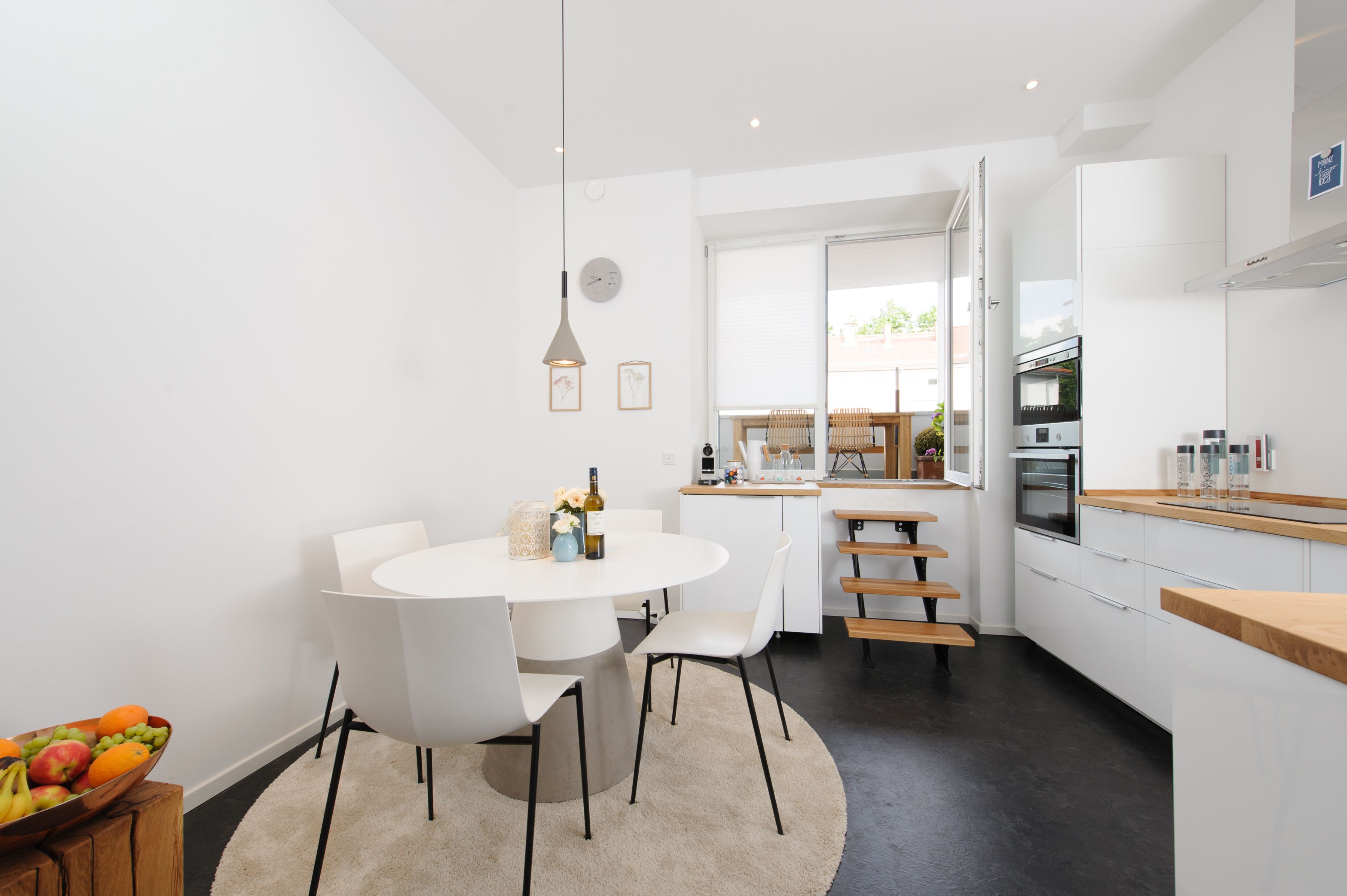 Una cocina moderna con armarios blancos, horno empotrado y zona de comedor con una mesa redonda y sillas.
