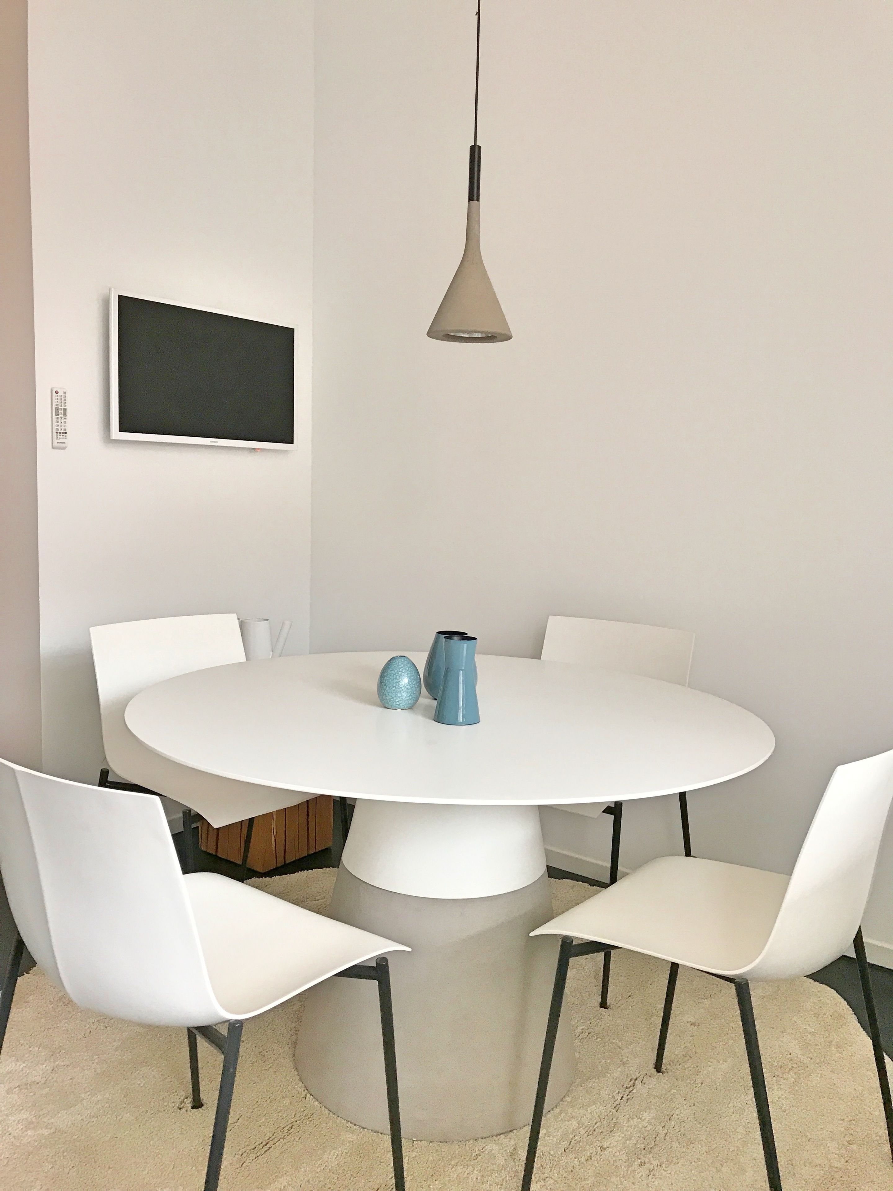A round dining table with four white chairs, a modern pendant light, and two decorative vases.