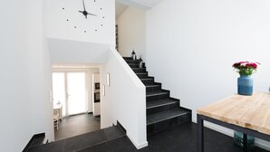 A modern staircase with black steps and white walls, leading to a room with a wooden table and a vase of flowers. - The Apartment Central (Mainz)