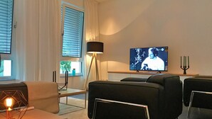 A modern living room with a flat-screen TV, a floor lamp, and a dining area with a table and chairs. - The Apartment Central (Mainz)