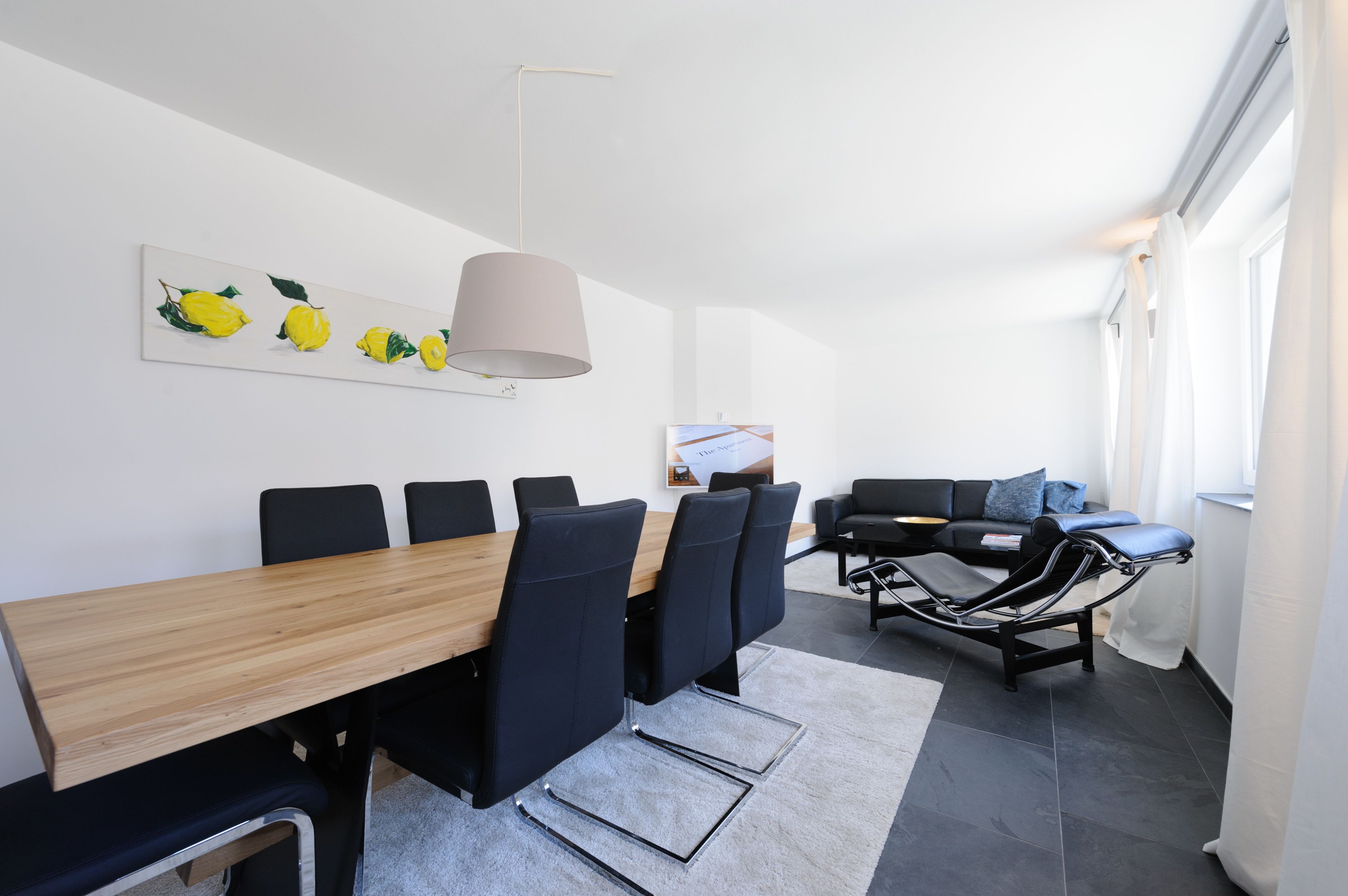 Una habitación moderna con una mesa de comedor de madera, sillas negras, un sofá negro y un sillón de masaje.