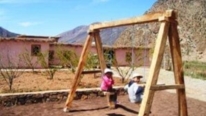 A wooden swing set in a desert environment with a building in the background. - Dar Aya Atlas (Ait Bou Oulli)