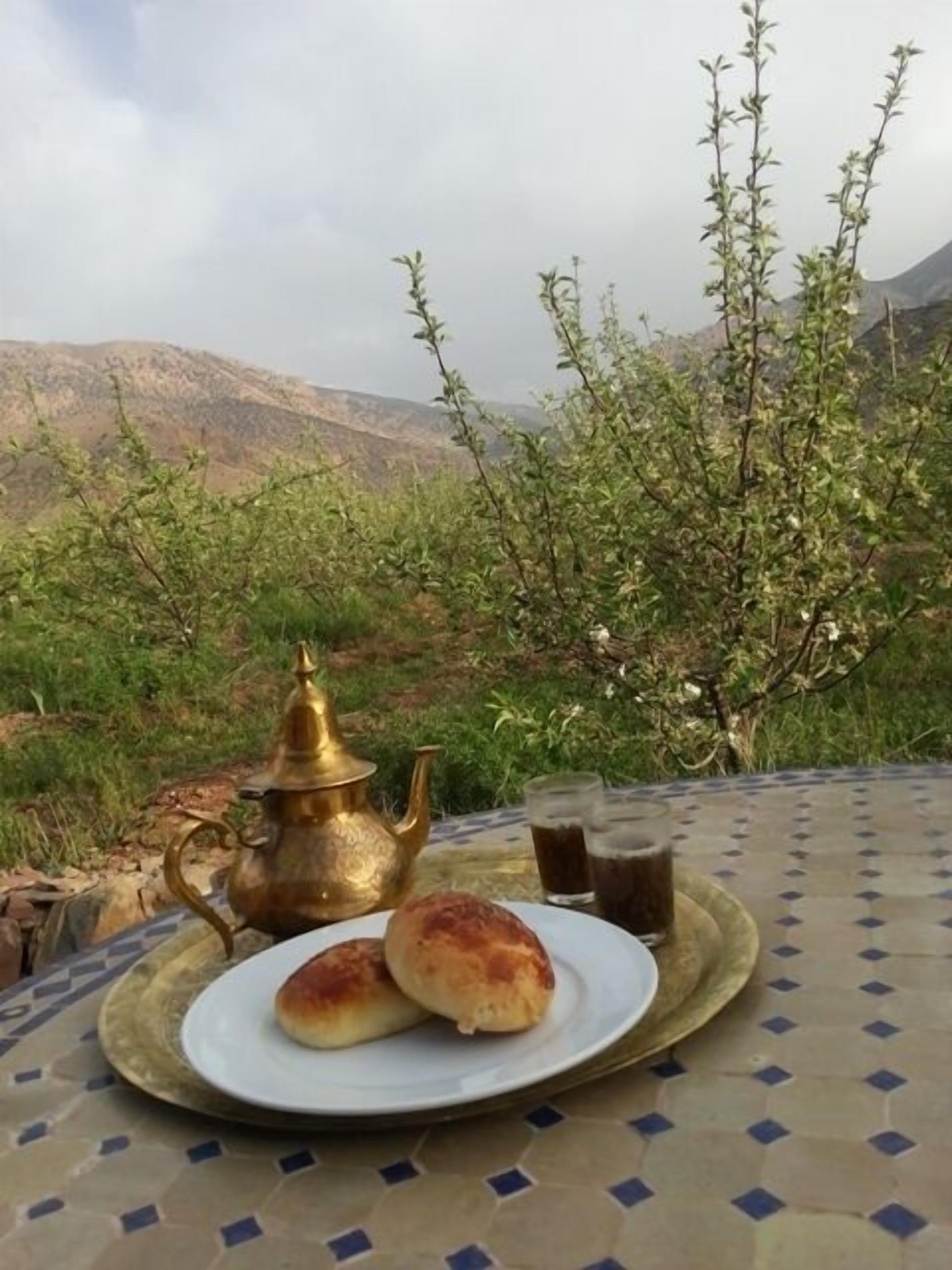 Ein Tisch mit Teekanne und zwei Gebäckstücken auf einer Serviertablette, vor einer Berglandschaft.
