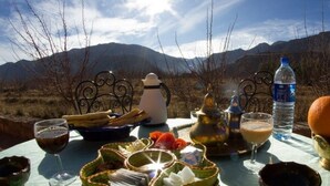 A table set outdoors with a view of mountains, including a water bottle, oranges, and various dishes. - Dar Aya Atlas (Ait Bou Oulli)