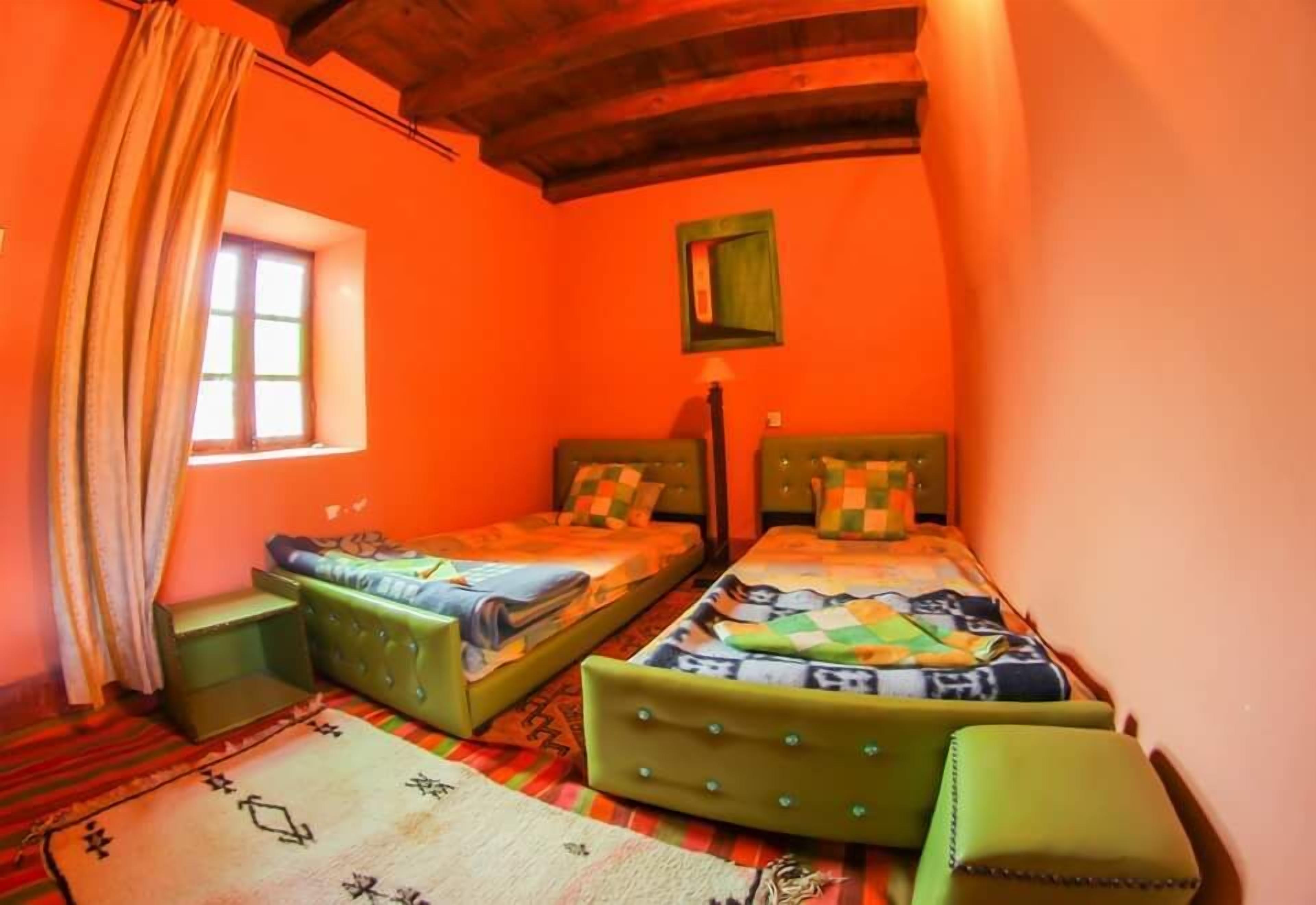 A small, cozy room with two beds, a window with curtains, and a wooden ceiling.